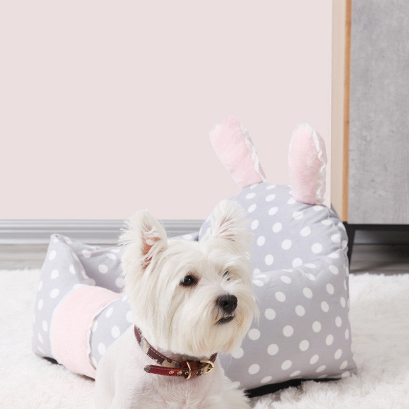 Small white dog sitting on a gray polka dot pet bed with pink interior.